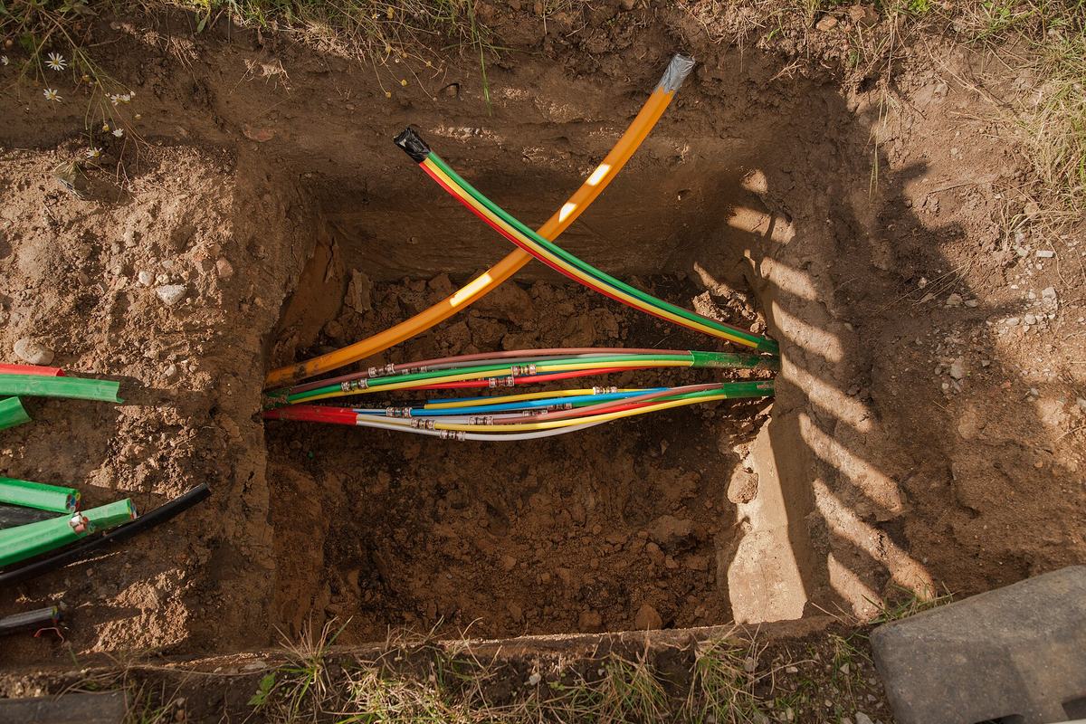 Een put met gekleurde telecombuizen in groen, geel en oranje die uit de grond komen